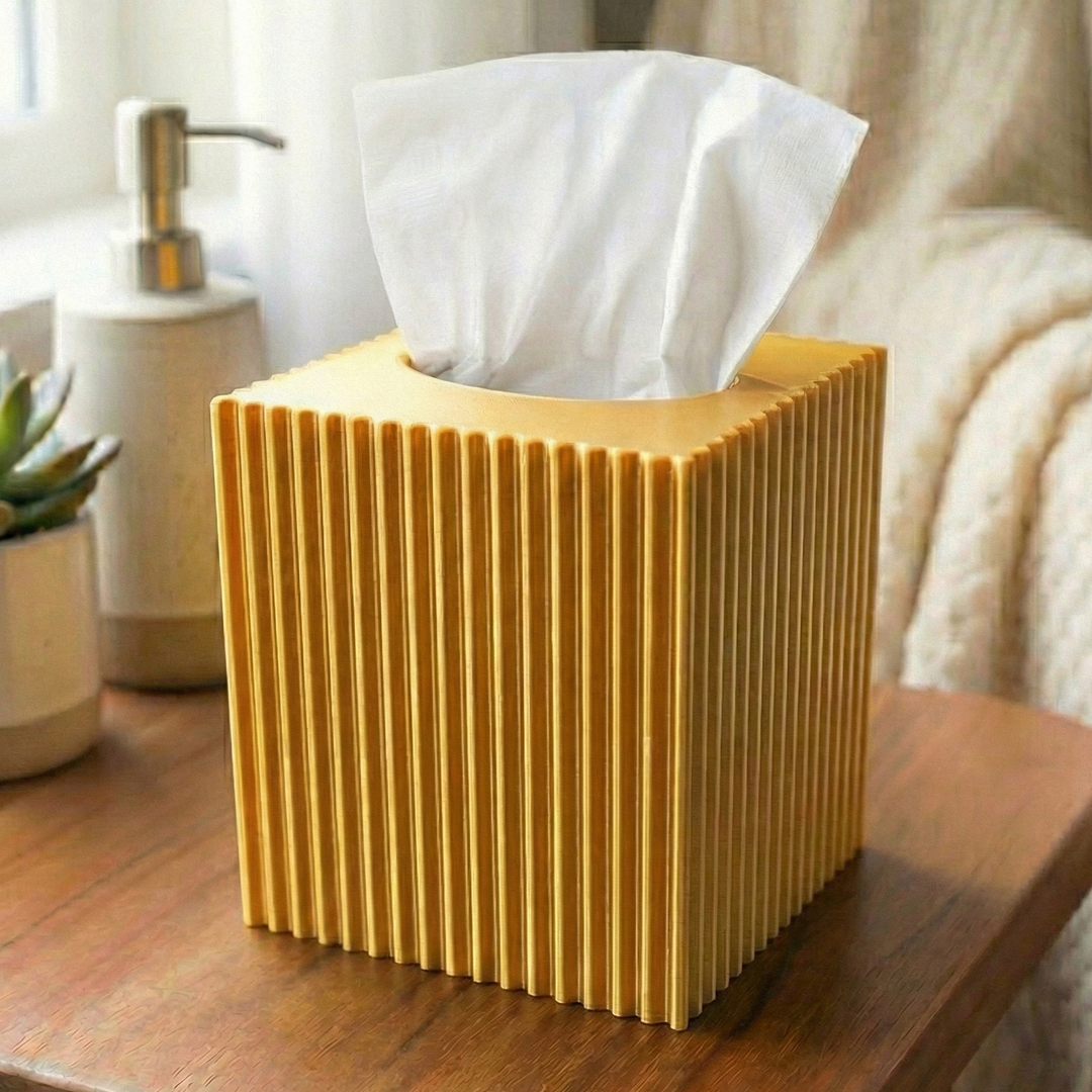 gold tissue box on a wooden table with a plant and soap dispenser in the background