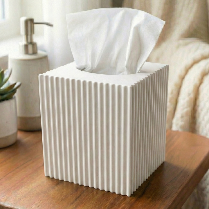 White ribbed tissue box on a wooden table with a plant and soap dispenser in the background.
